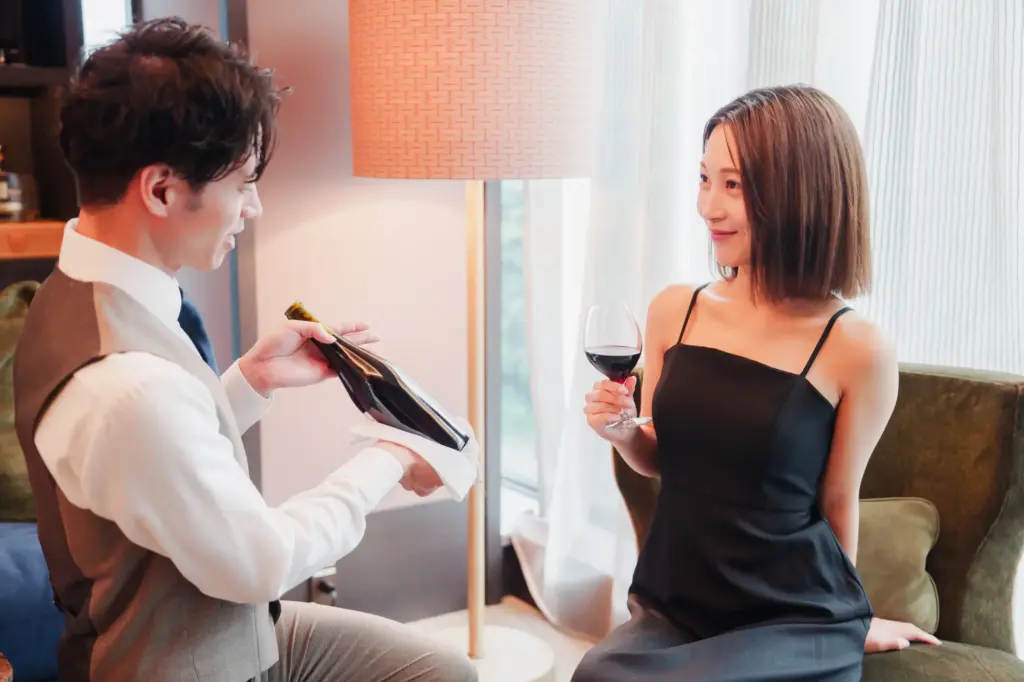 ホテルのルームサービスで女性にワインを提供する男性ソムリエ